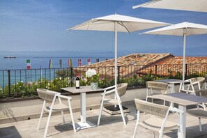 An outdoor terrace with white tables and chairs, umbrellas, and a view of the sea. - I Tre Re (Bardolino)
