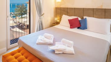 Habitación de hotel con cama, vista al mar y balcón con mesas y sillas.