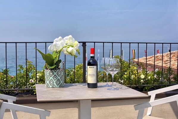 A table with a bottle of Masi wine and a glass, a potted plant, and a view of the sea. - I Tre Re (Bardolino)