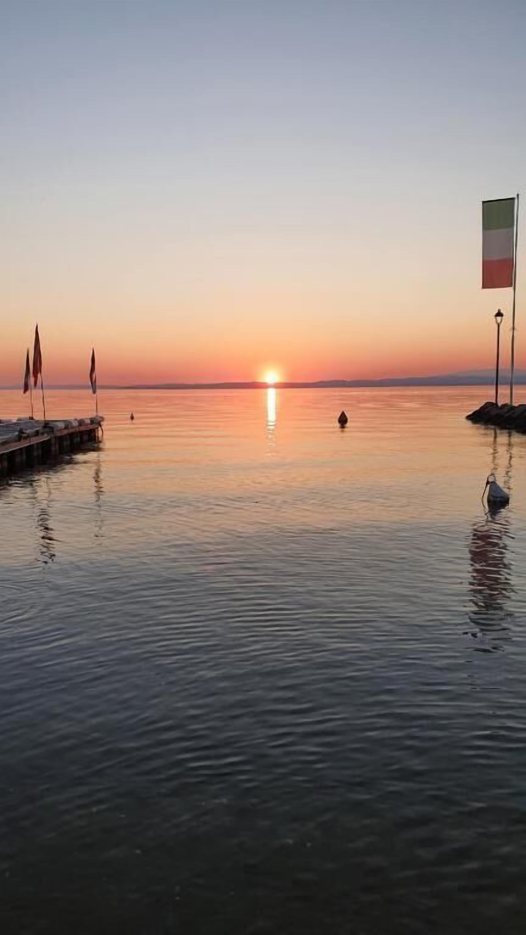 A calm sunset over a body of water with a pier and a flag.