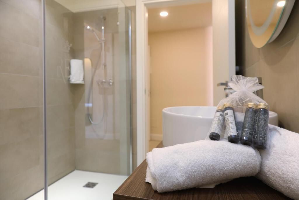 Un baño moderno con ducha envuelta en vidrio, lavamanos blanco y toallas ordenadas sobre una superficie de madera.