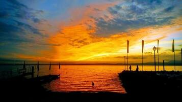 A sunset over a body of water with a pier and flags.