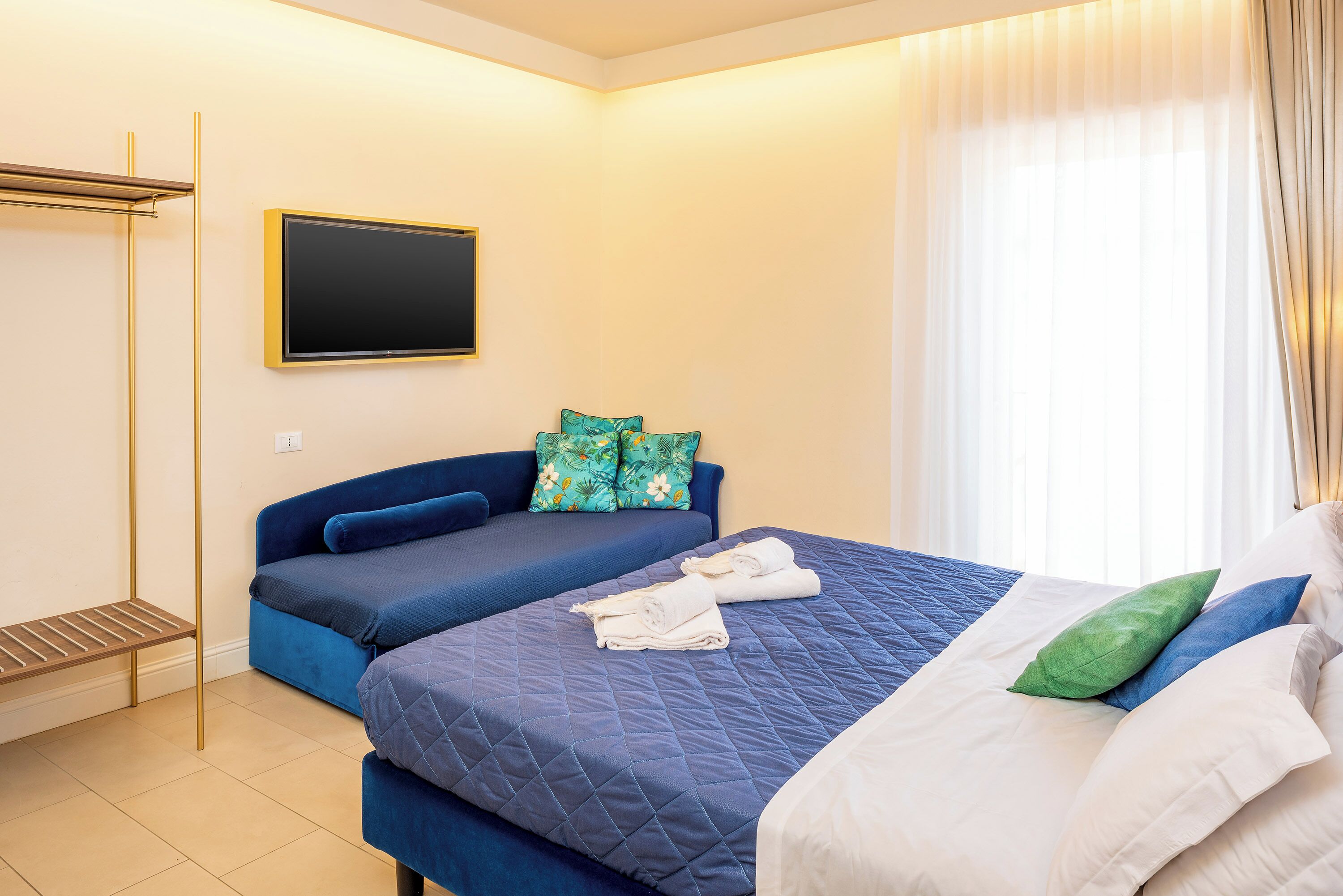 Ein Hotelzimmer mit Bett, Sofa, Fernseher und einem Vorhangfenster.