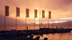 A marina with boats docked and flags on poles, with a sunset in the background. - I Tre Re (Bardolino)