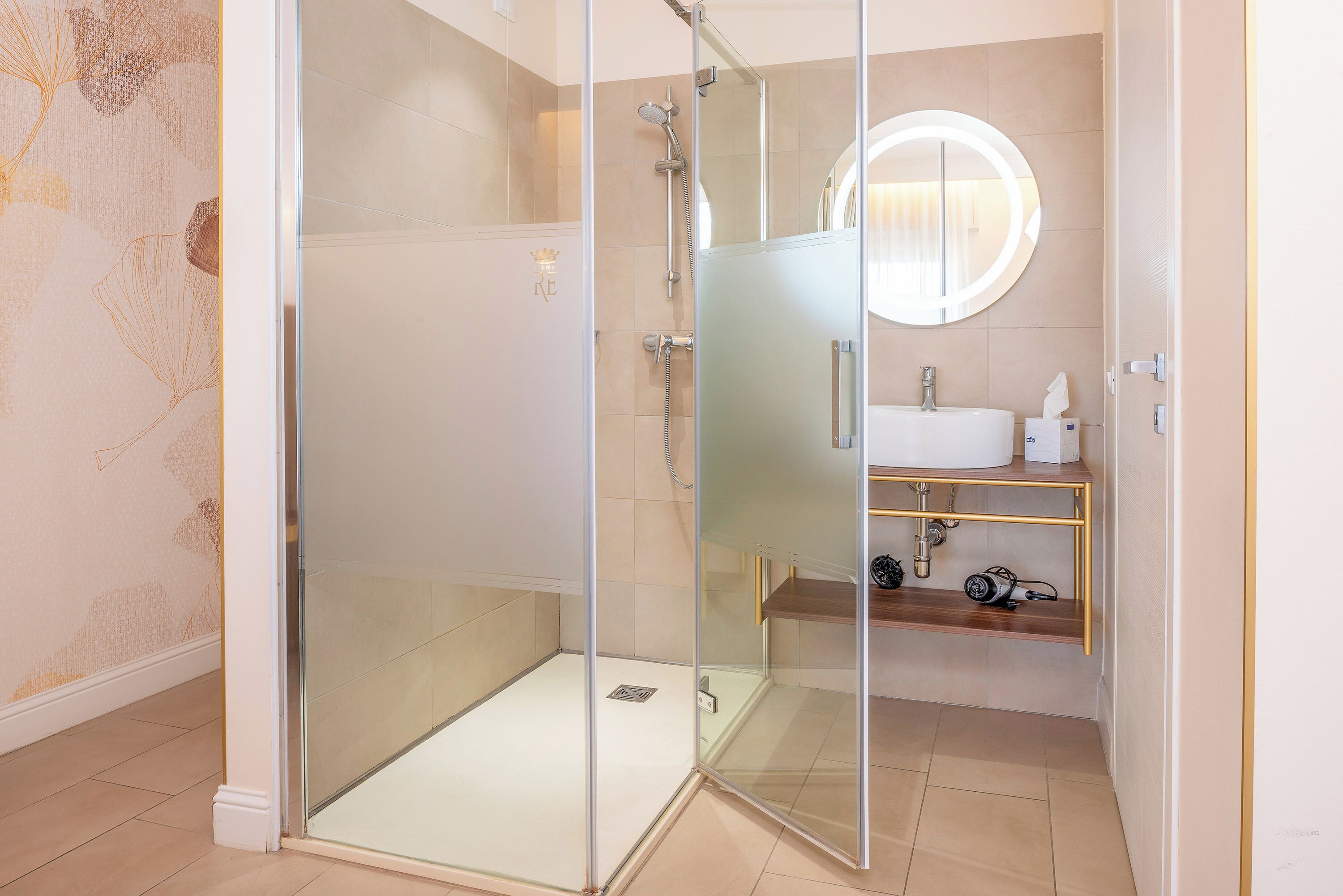 Ein modernes Badezimmer mit einer gläsernen Duschkabine, einem runden Spiegel und einem Waschbecken mit Handtuchspender.
