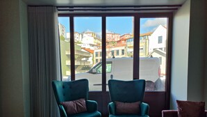 A room with two teal armchairs, a wooden floor, a large window with a view of buildings, and a pink sofa. - Fervença Apartments - Corgo (Vila Nova de Gaia)