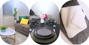Un comedor con una mesa preparada para cuatro, un sofá con cojines y una mesita redonda con una planta y dos tazas.