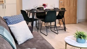 A modern living room with a sofa, a dining table set for four, and a wooden door in the background. - Charming 1-bed, Sleeps 2, Parking (Leeds)