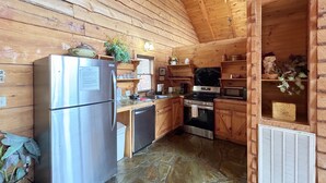 Uma cozinha de cabana de madeira com uma geladeira de aço inoxidável, um fogão e um micro-ondas.