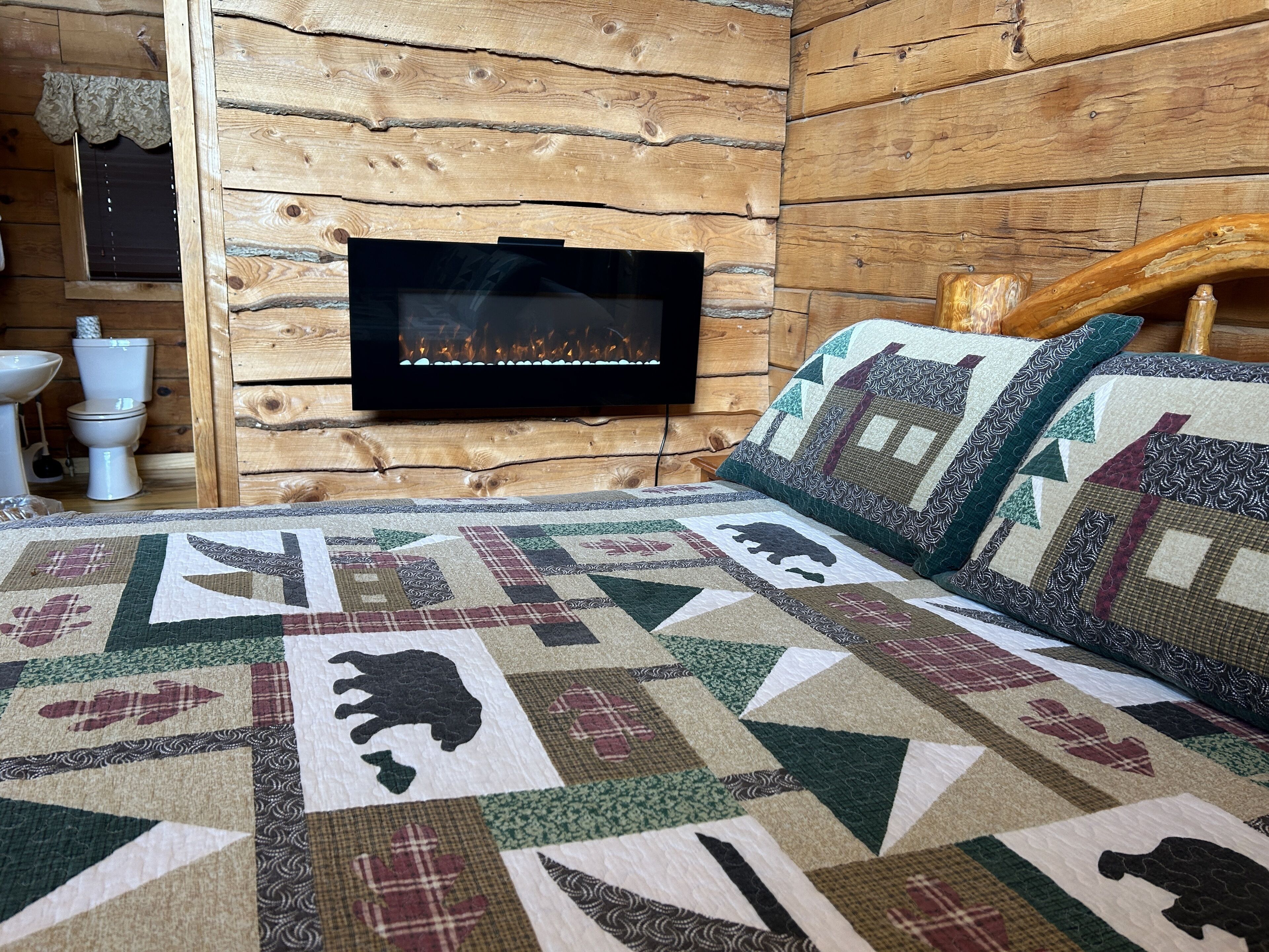 A log cabin room with a fireplace, a bed with a quilt, and a wooden headboard.