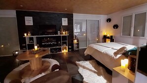 Ein modernes Hotelzimmer mit einem großen Bett, einem Fernseher, einer Sitzecke mit Tisch und Stühlen sowie einem Kamin.