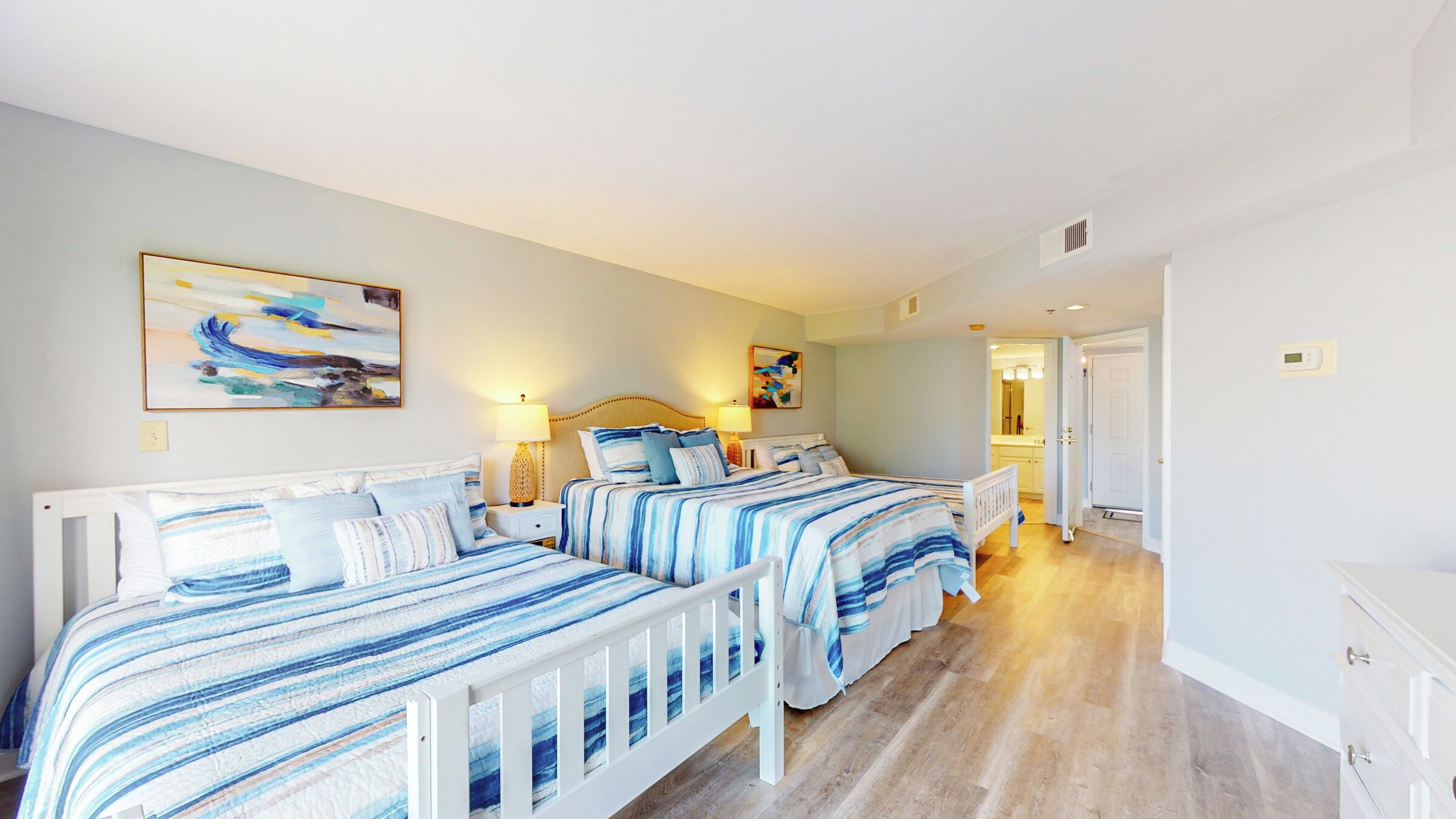 A bedroom with two beds, a nightstand, a lamp, and a painting on the wall.