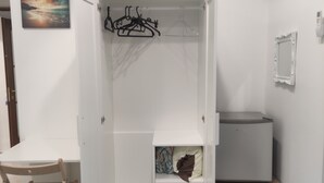 A room with a white wardrobe, a wooden chair, a small table, and a trash bin.