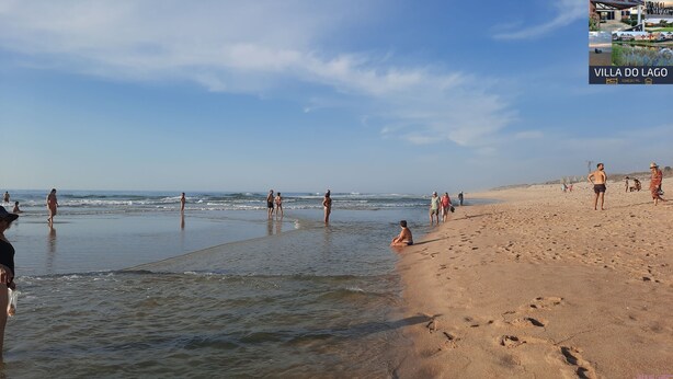 A beach with people walking and standing in the water.