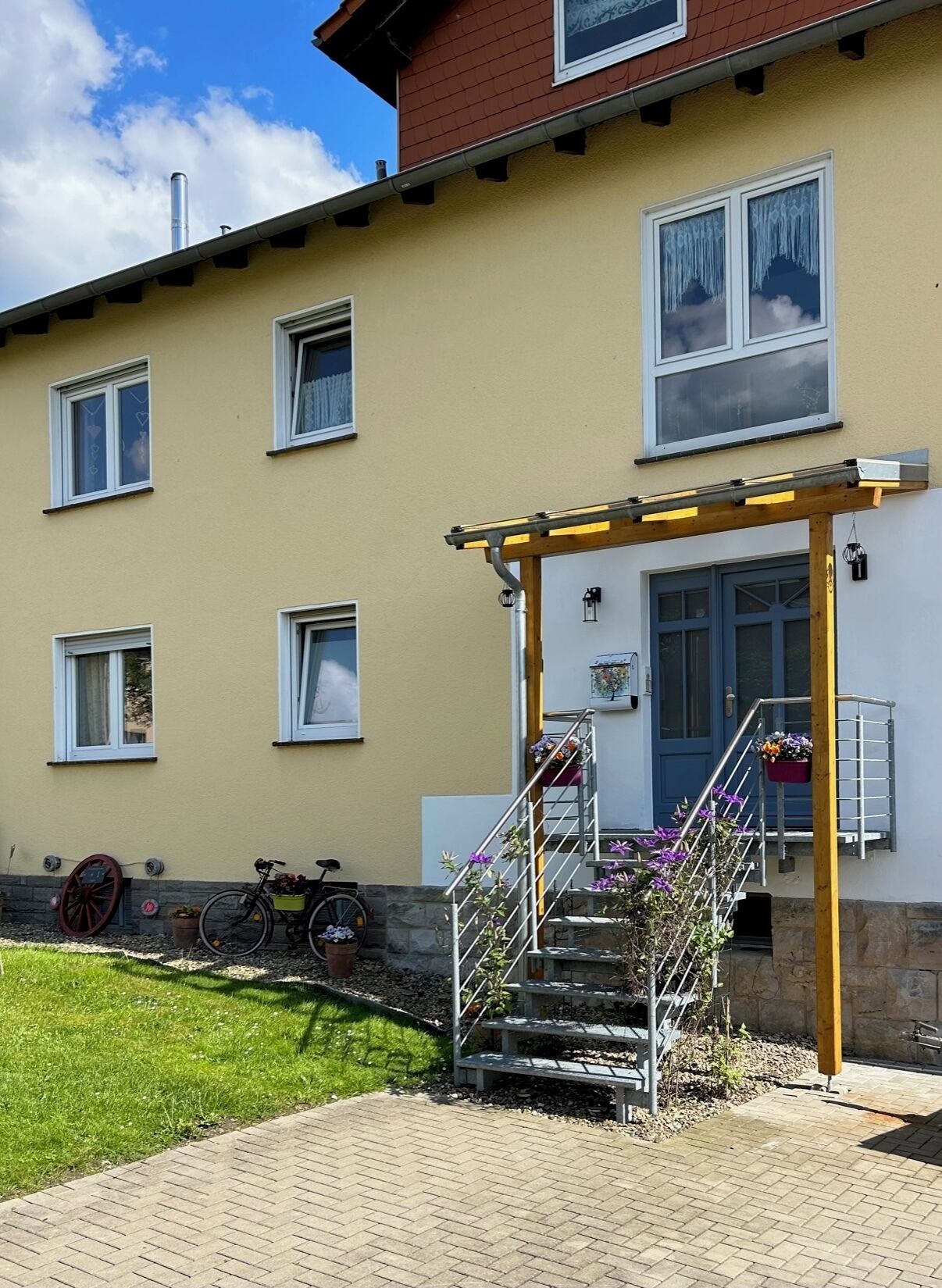 Ein Gebäude mit gelber Fassade, zahlreichen Fenstern, einer Holzpergola und einer Treppe, die zu einer Tür führt.