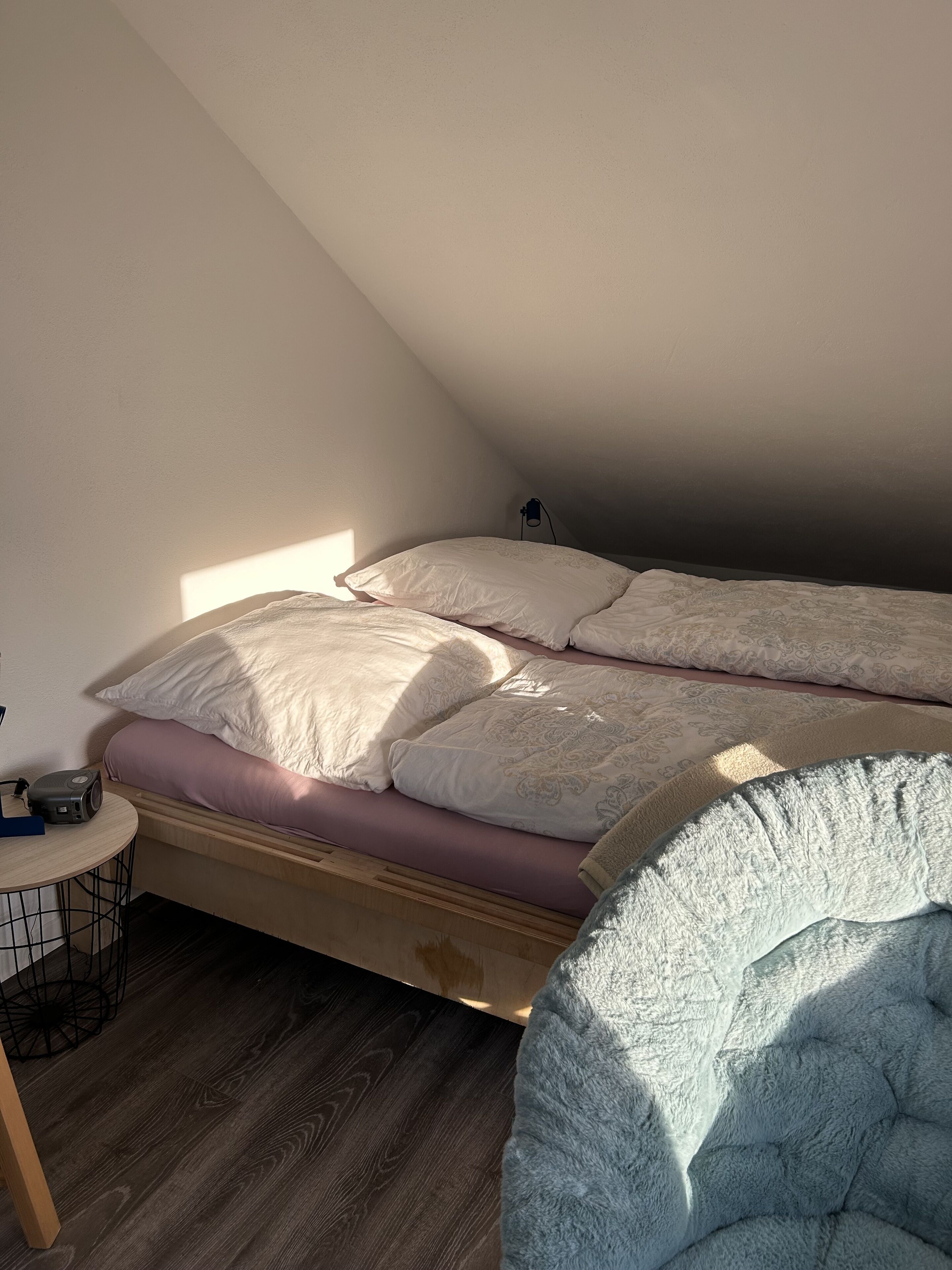Une chambre avec un plafond en pente, un lit avec de nombreux oreillers, une petite table ronde avec une lampe et une chaise.