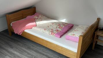 Una habitación pequeña con cama individual, estructura de madera, suelo estampado en gris y techo inclinado.