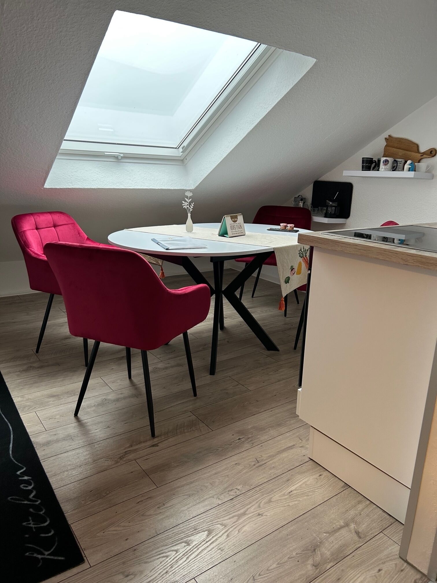 A modern kitchen with a skylight, a dining area with red chairs, and a kitchen counter.
