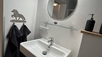 Ein Badezimmer mit einem weißen Waschbecken, einem runden Spiegel, einer Glasablage und einem Handtuchhalter mit Pferdeanhänger.