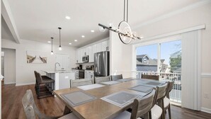 Une cuisine moderne avec des armoires blanches, des appareils en acier inoxydable et un coin repas comprenant une grande table et des chaises.