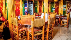 Un comedor tradicional de madera con sillas tejidas y una mesa redonda, decorado con motivos coloridos y una máquina expendedora de Pepsi.