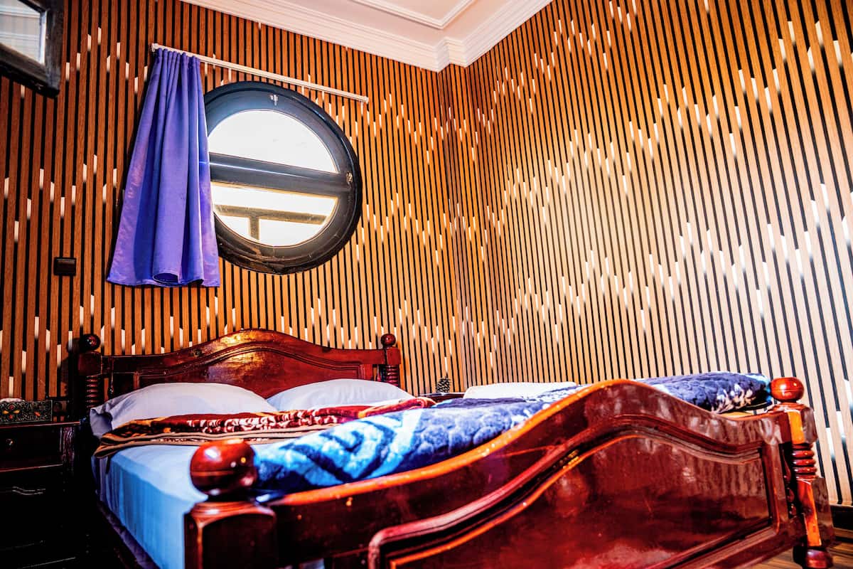 A wooden-paneled room with a bed, a round window, and a curtain.