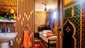 Habitación de hotel con una cama, una mesita de noche, un estante en la pared con artículos de aseo y una puerta decorativa.
