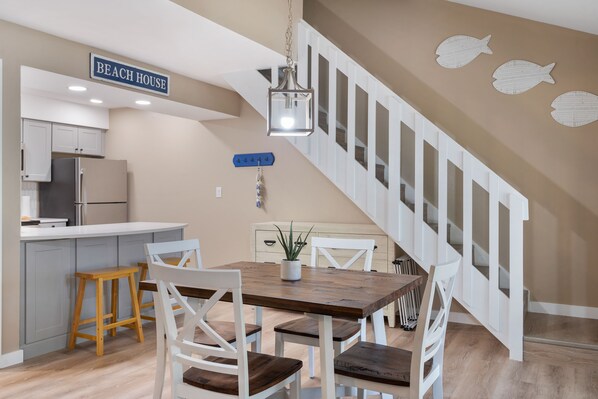A kitchen with white cabinets, a wooden dining table, and a staircase with white railings.
