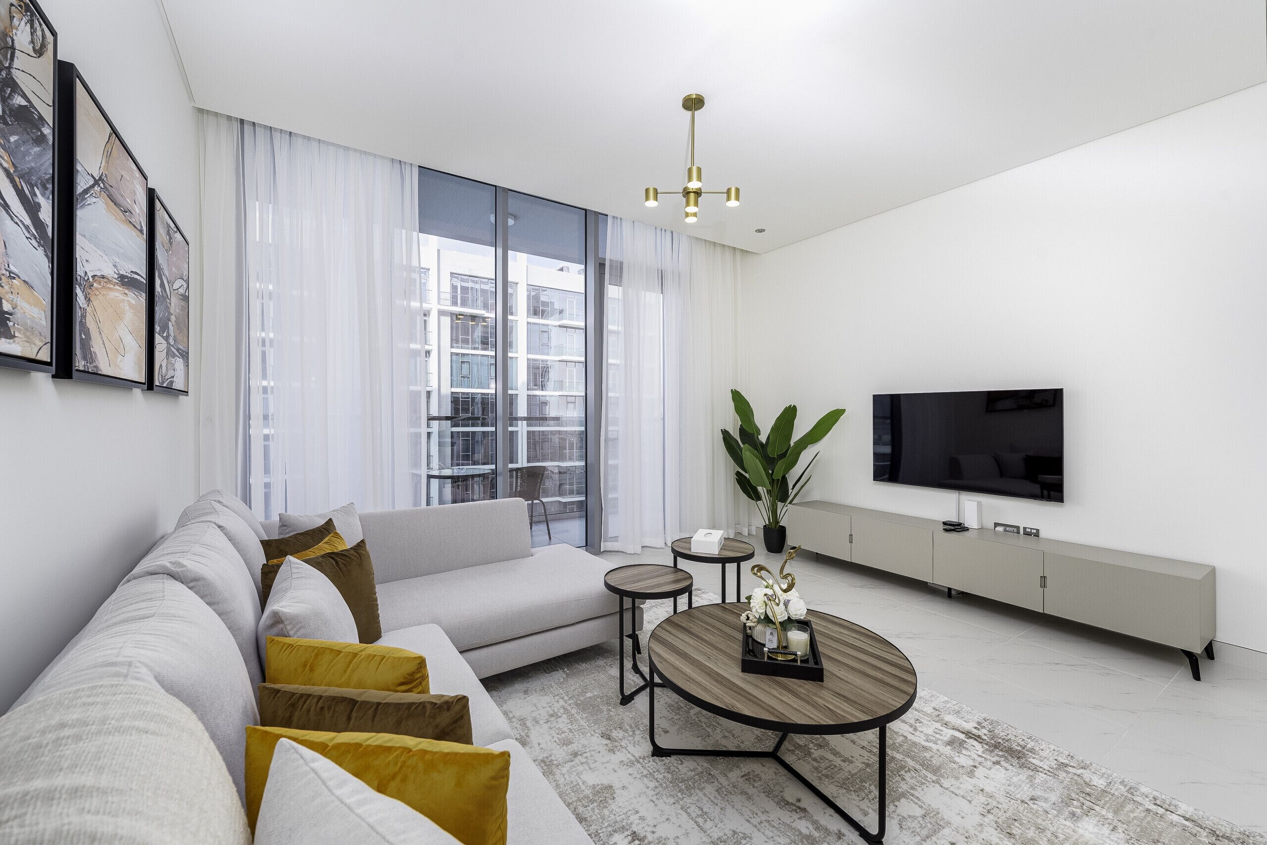 Una sala de estar moderna con un sofá, una mesa de centro, televisor y ventanas amplias.