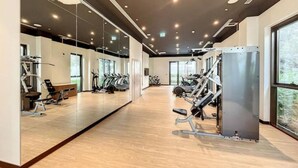 A spacious gym with cardio machines, weight equipment, and large windows offering natural light.