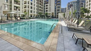 A swimming pool with lounge chairs and umbrellas, surrounded by multi-story buildings with balconies.