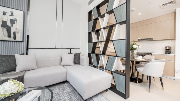 A modern living room with a sectional sofa, a glass coffee table, and a decorative wall panel.