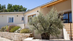 A building with a stone wall, a large bush, and a staircase leading to a balcony. - Villa in Provence with pool, garden and Ventoux view – Colonzelle (Colonzelle)