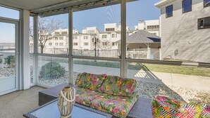 Un porche cubierto con un sofá de colores y una mesa de mimbre, con vistas a una zona residencial con casas y una cerca.