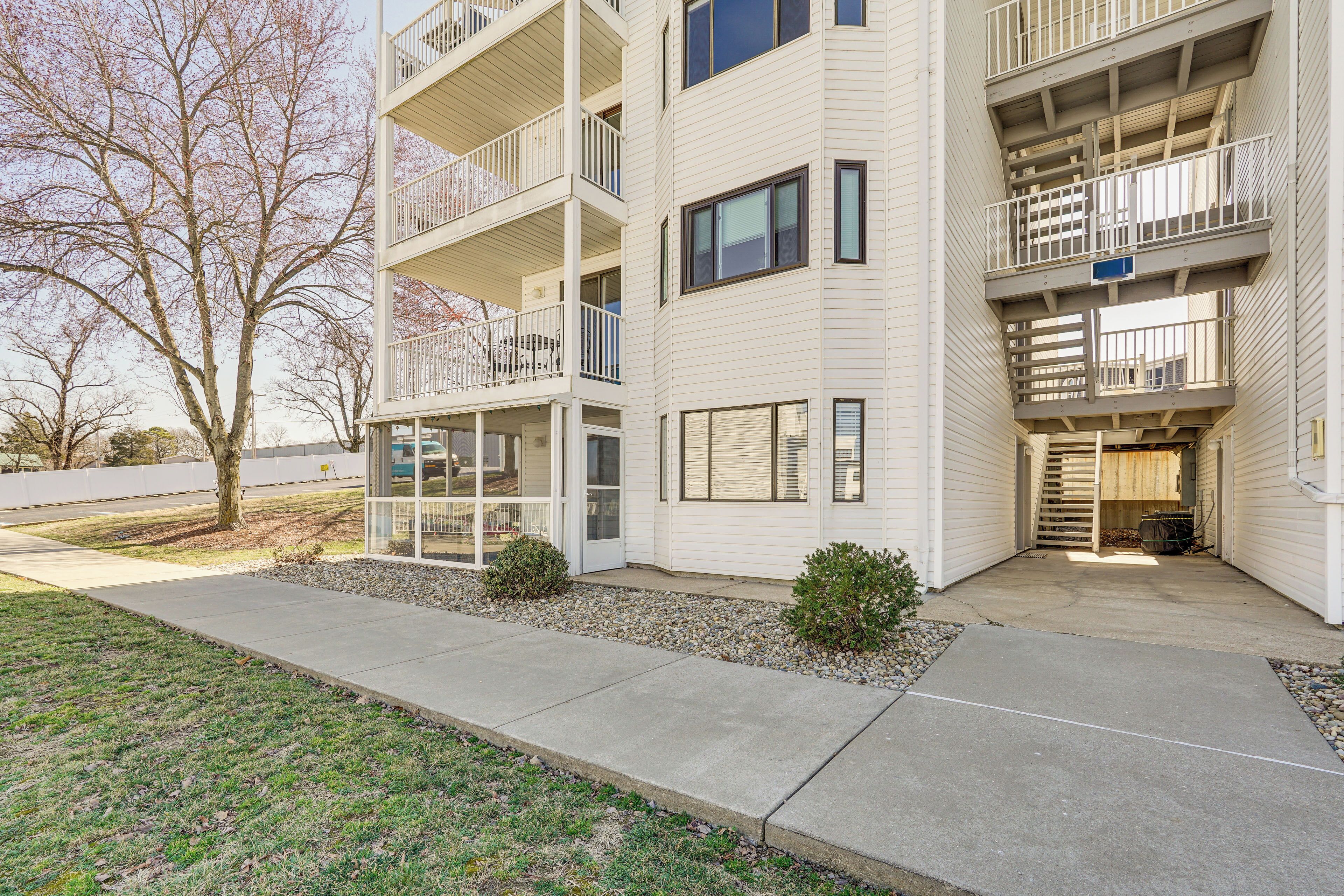 A multi-story residential building with balconies, a covered entryway, and a small garden area.