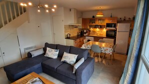 A living room with a sofa, a dining table with chairs, a kitchen area with appliances, and a staircase. - L'Escapade Charentaise, a quiet getaway with swimming pool (LA TREMBLADE)