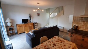 A modern living room with a sofa, a TV, and a dining table with a patterned tablecloth. - L'Escapade Charentaise, a quiet getaway with swimming pool (LA TREMBLADE)