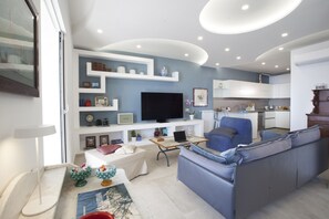 A modern living room with a sofa, a coffee table, a TV, and a bookshelf. - AMORE RENTALS - Villa Domus Franca with Seafront Shared Pool (Massa Lubrense)