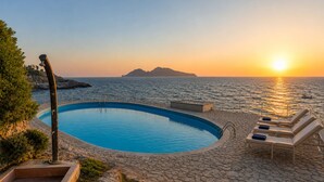 En pool med solstolar och utsikt över havet vid solnedgången.