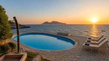 Una piscina con lettini e vista sul mare al tramonto.