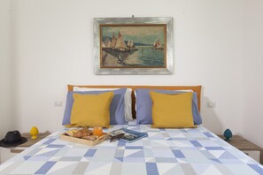 A bed with a geometric patterned bedspread, two pillows, a tray with bread and orange juice, a book, and a framed painting of sailboats on the wall.