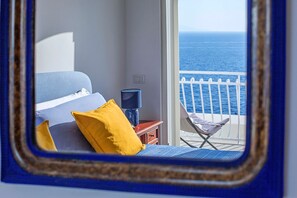 Un dormitorio con cama, mesita de noche, lámpara y vista al mar a través de la barandilla del balcón.