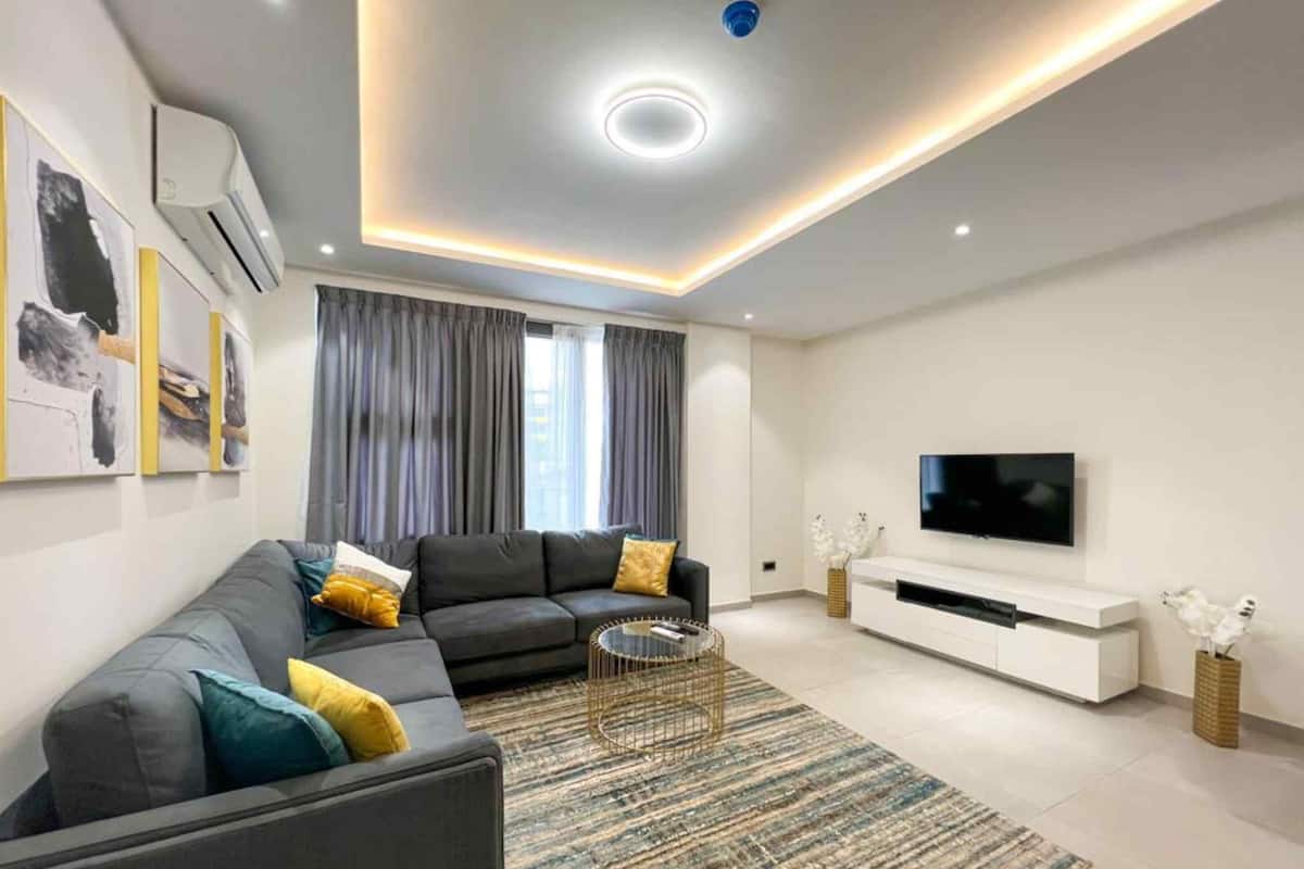 A modern living room with a sectional sofa, a flat-screen TV, and a minimalist white entertainment unit.