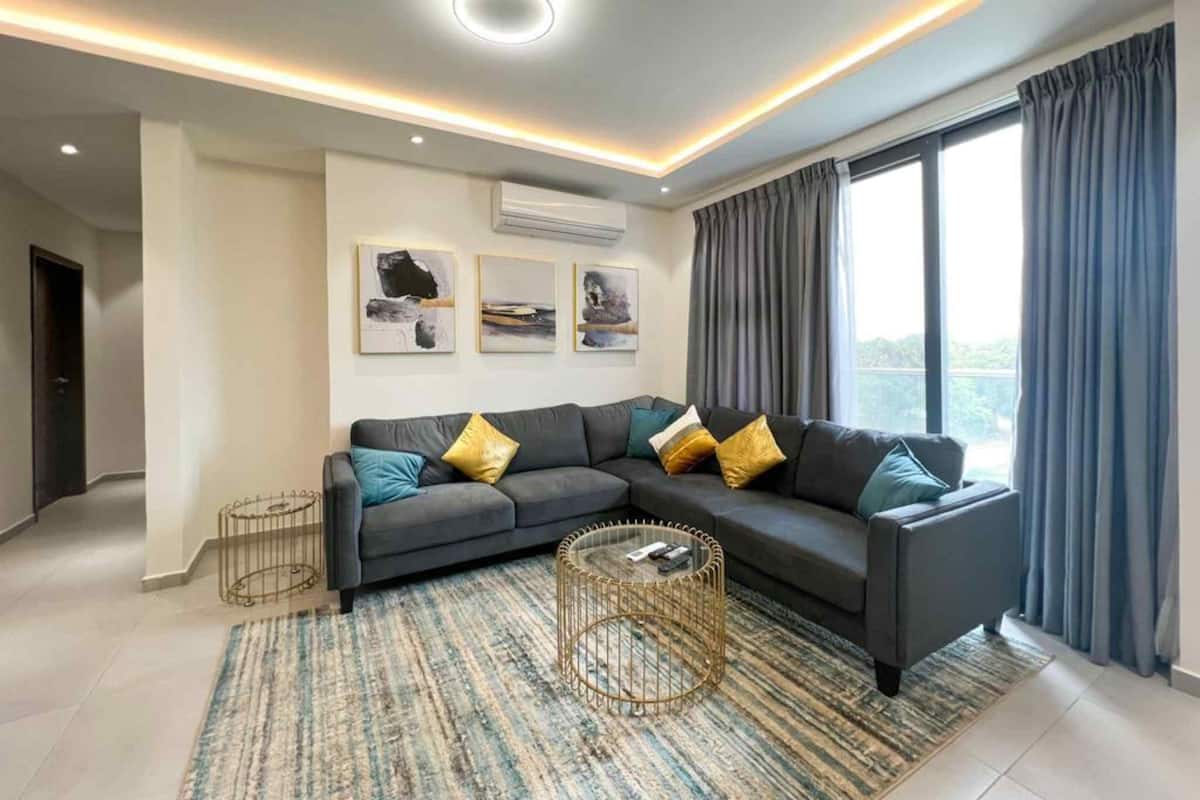 A modern living room with a sectional sofa, a round coffee table, and a large window with curtains.