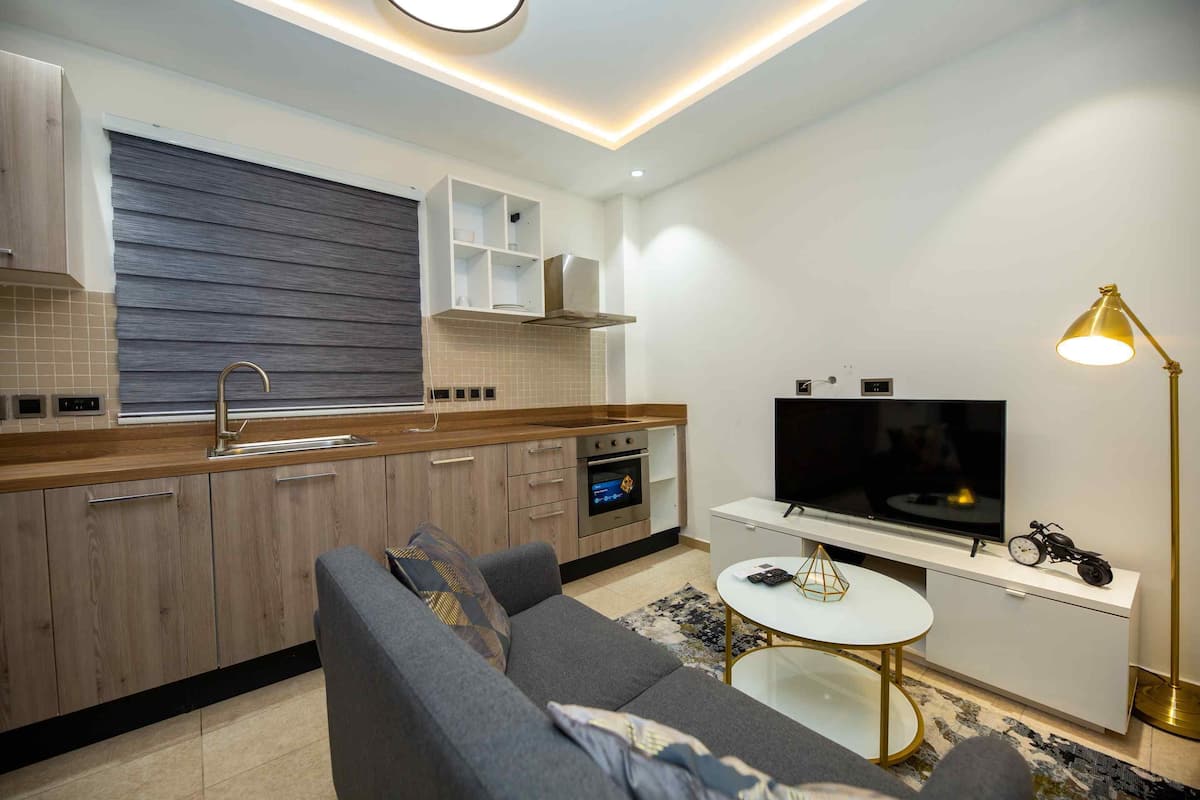 A modern kitchen with wooden cabinets, a built-in oven, and a large flat-screen TV.