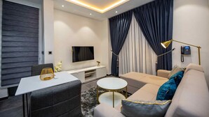 A modern living room with a flat-screen TV, sofa, coffee table, and a dining area with a white table and chairs.
