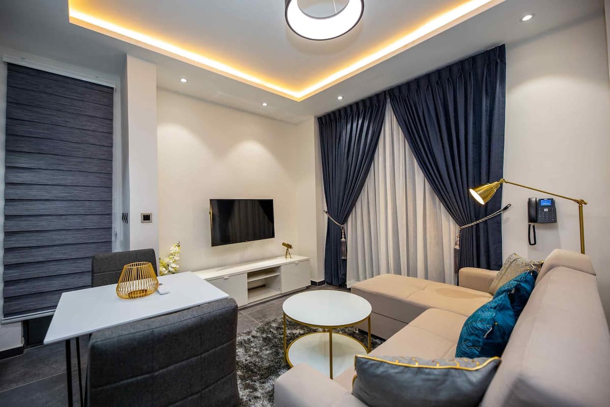 A modern living room with a flat-screen TV, sofa, coffee table, and a dining area with a white table and chairs.
