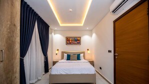 A modern bedroom with a bed, curtains, a painting, and a wooden door.