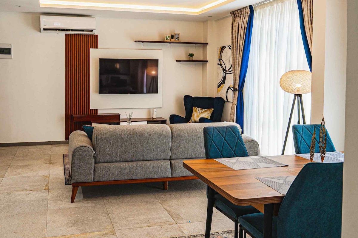 A modern living room with a sofa, a TV, a dining table, and a lamp.
