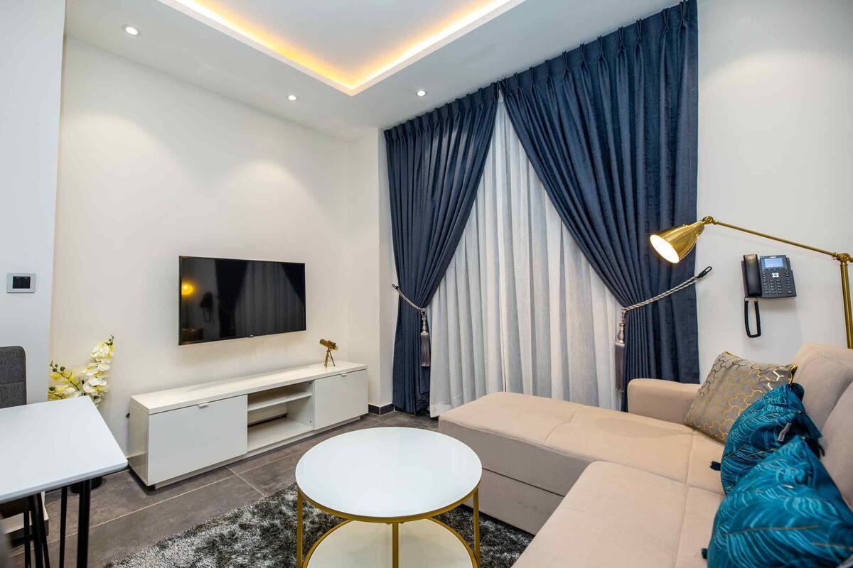A modern living room with a flat-screen TV, a sofa, a coffee table, and a lamp.